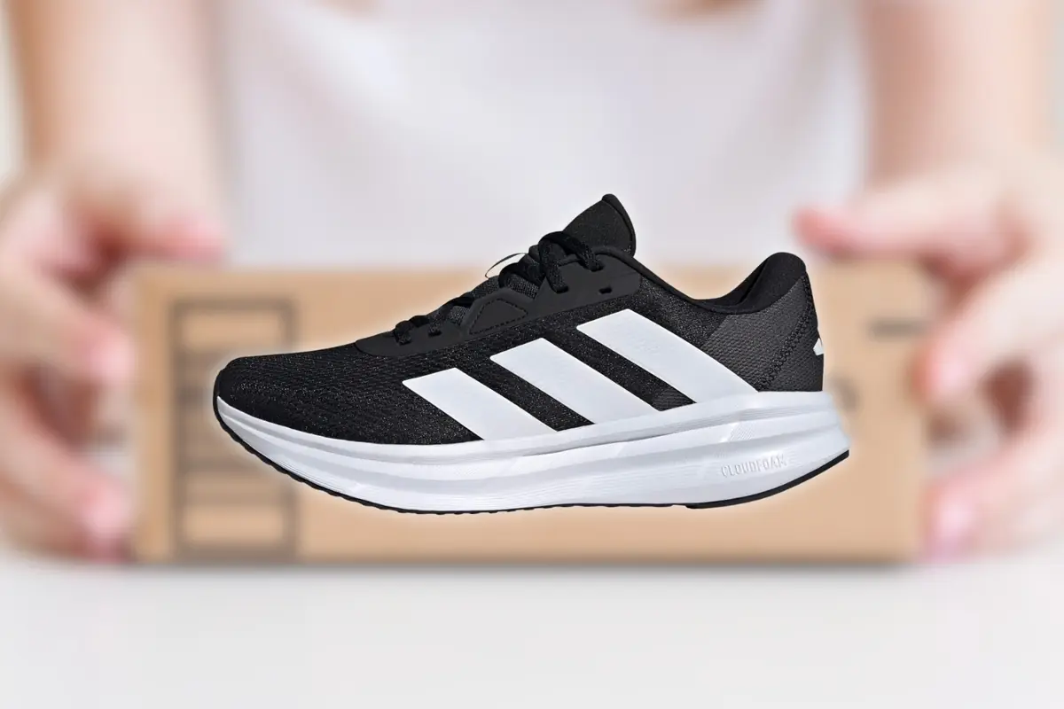 Montaje con zapatilla deportiva negra con suela blanca y tres franjas blancas en el lateral sobre fondo desenfocado con caja de envío