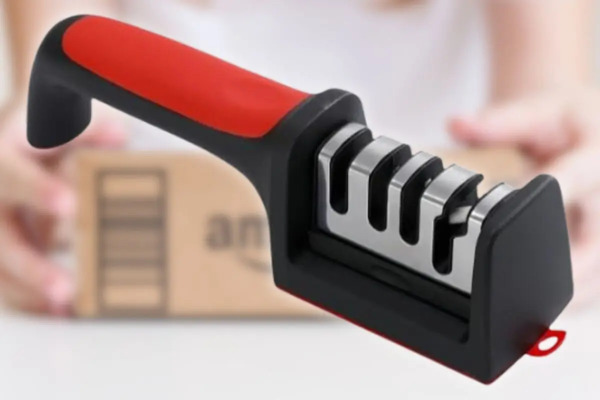 Afilador manual de cuchillos negro y rojo con ranuras metálicas sobre una caja de cartón desenfocada de fondo