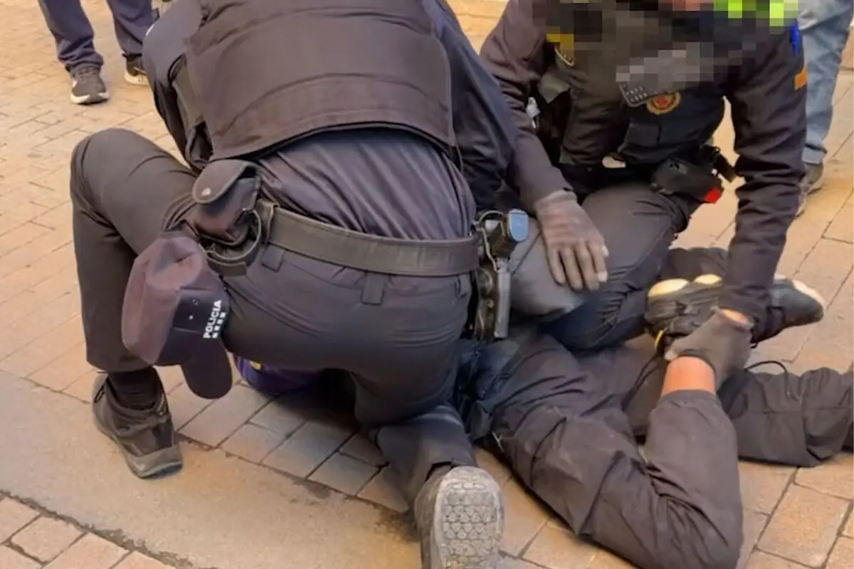 Diversos agents de policia immobilitzen a terra una persona emmanillada durant una detenció a la via pública
