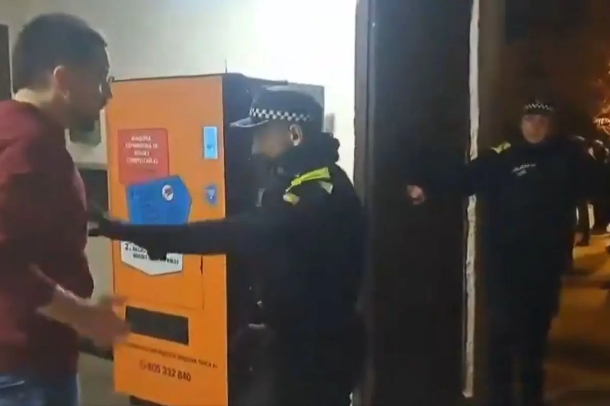 Policías municipales detienen a un hombre frente a una máquina expendedora en una calle de noche