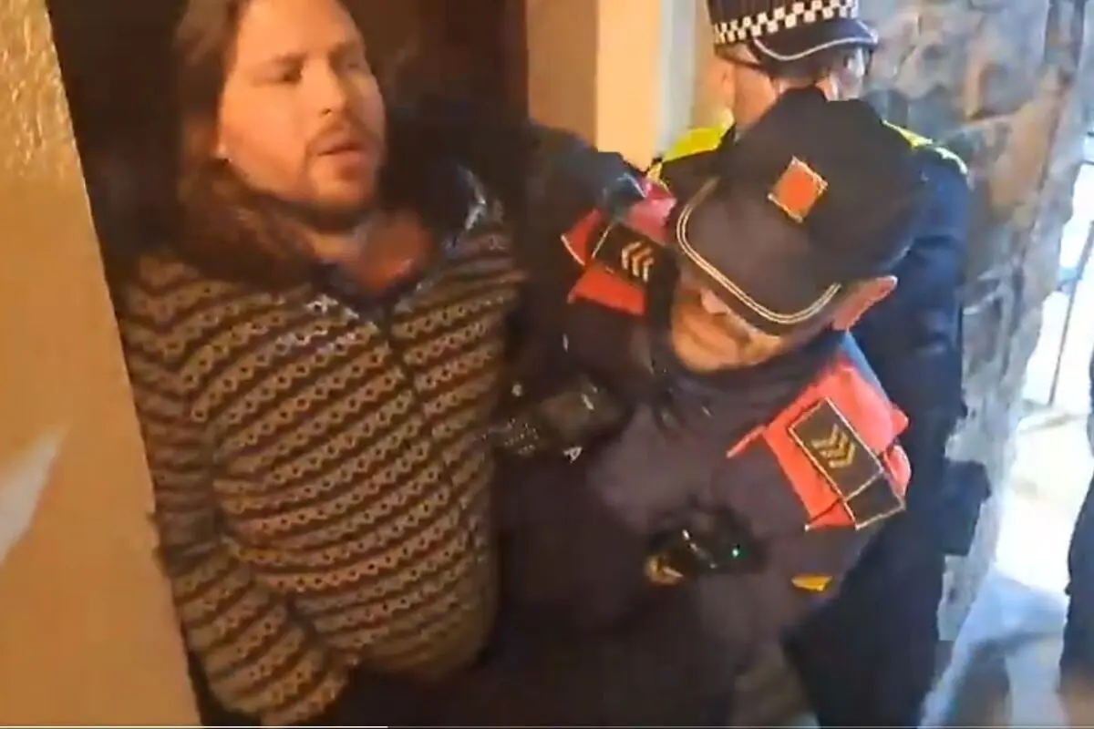 Agentes de policía sacan a un hombre de una vivienda sujetándolo por los brazos mientras lo escoltan hacia la salida