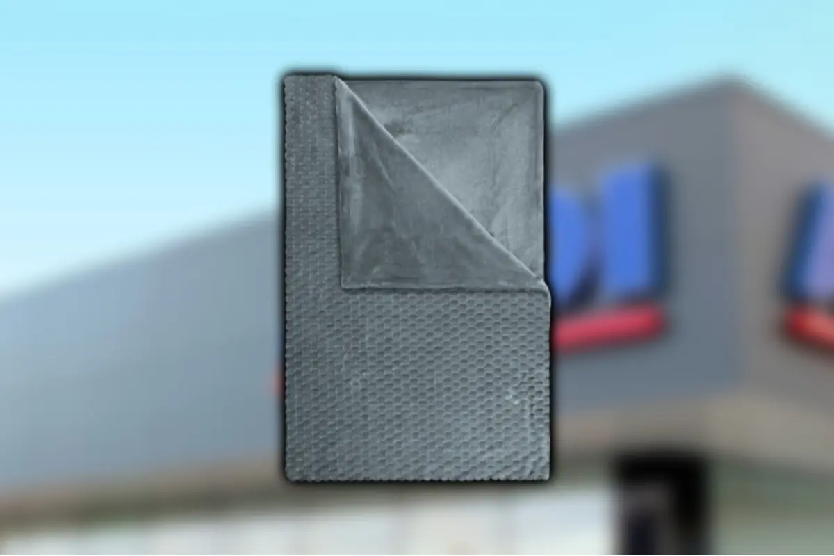 Manta gris de textura acolchada doblada y superpuesta sobre un fondo desenfocado de edificio comercial