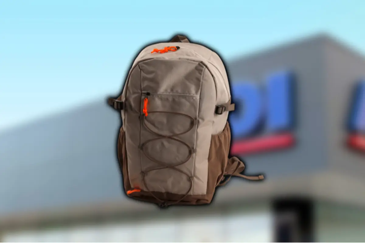 Mochila de senderismo beige y marrón con detalles naranjas sobre fondo de tienda desenfocado