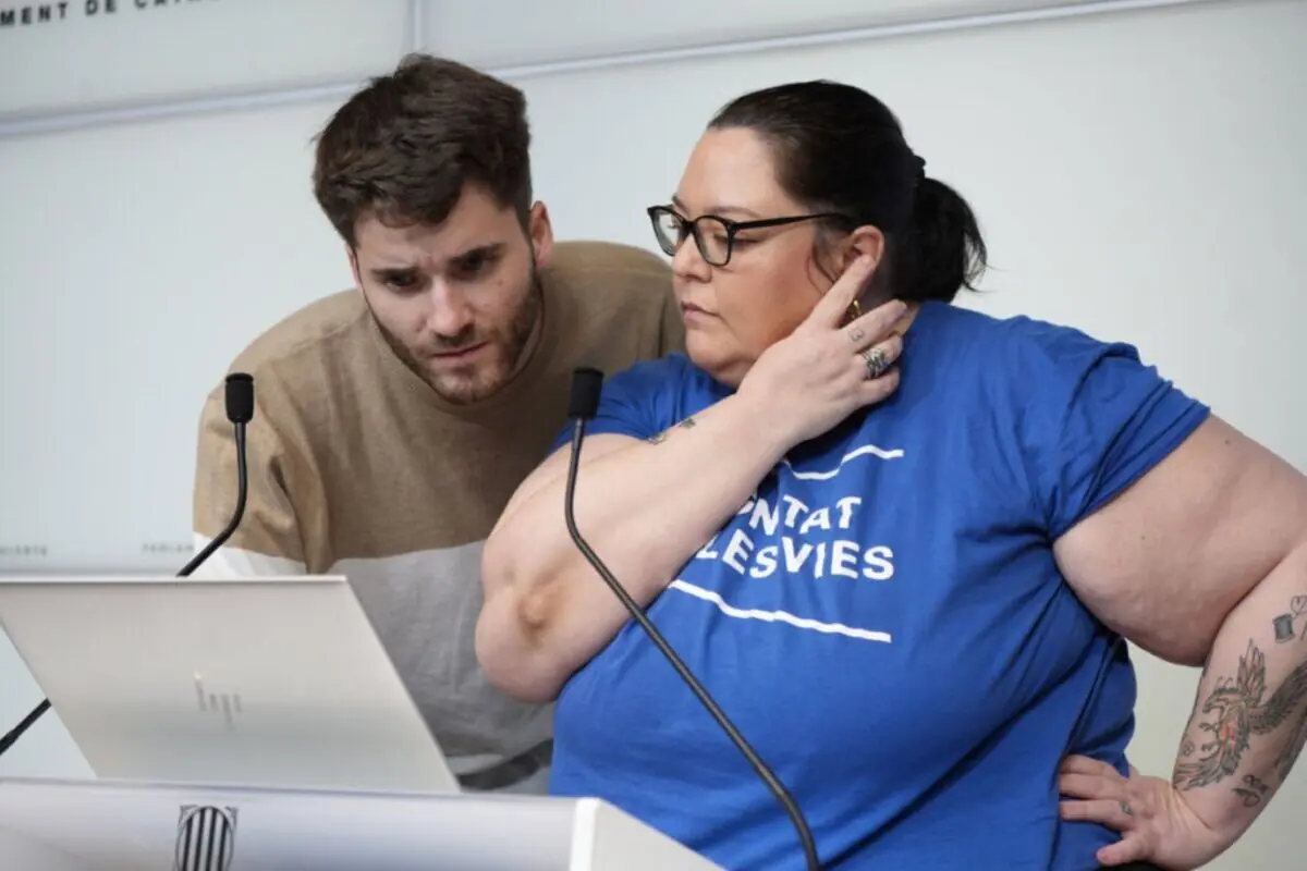 Dues persones revisen concentrades la pantalla d’un portàtil en un faristol de conferència mentre es preparen per parlar en públic