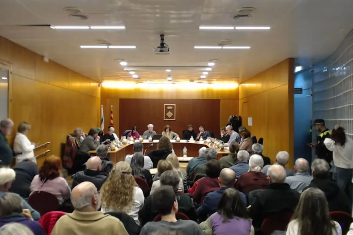 Sala de plens municipal plena de persones assistents mentre regidors i autoritats seuen en una taula en forma d’U al fons de la sala Sala de plens municipal plena de persones assistents mentre regidors i autoritats seuen en una taula en forma d’U al fons de la sala