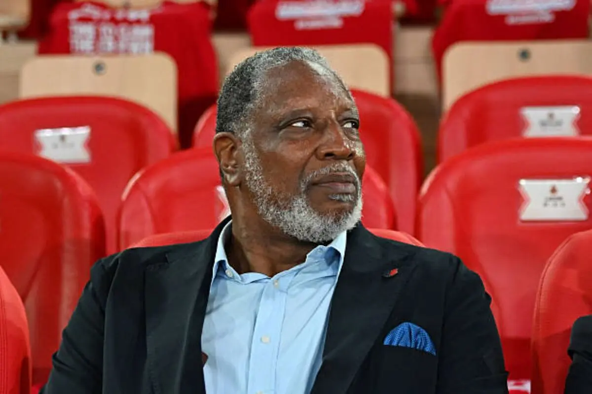 Home gran amb barba encanecida i vestit fosc assegut en una grada de seients vermells mirant cap a un costat