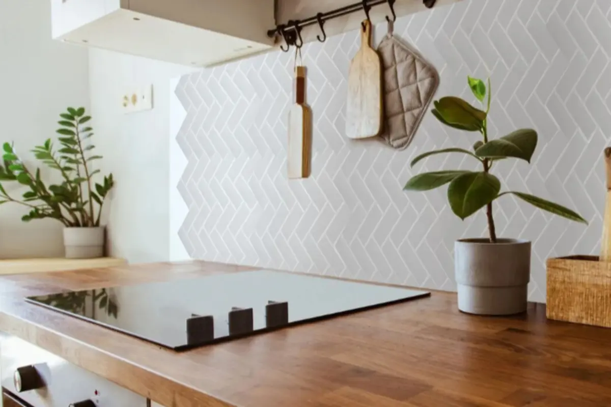 Wooden kitchen countertop with a black induction cooktop, potted plants, and a wall with white herringbone tiles and hanging utensils