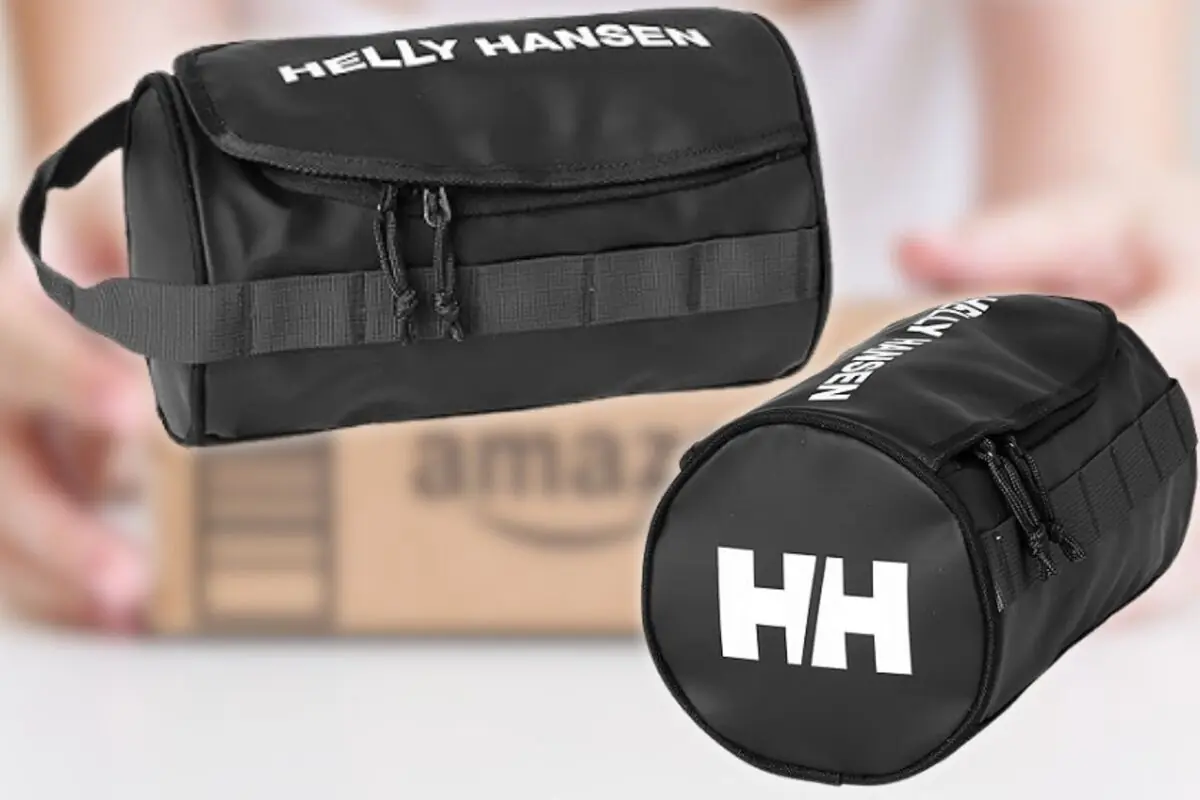 Neceser cilíndrico negro Helly Hansen con cremallera y asa de mano sobre fondo desenfocado con caja de envío