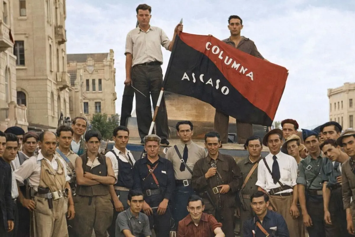 Grup de milicians posant en un carrer al costat d’una bandera vermella i negra amb el text Columna Ascaso.