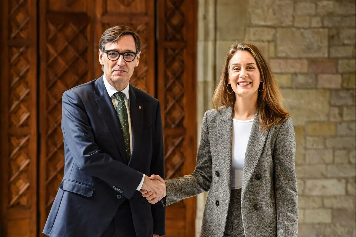 Home i dona amb vestit donant-se la mà i somrient davant d’una porta de fusta i una paret de pedra