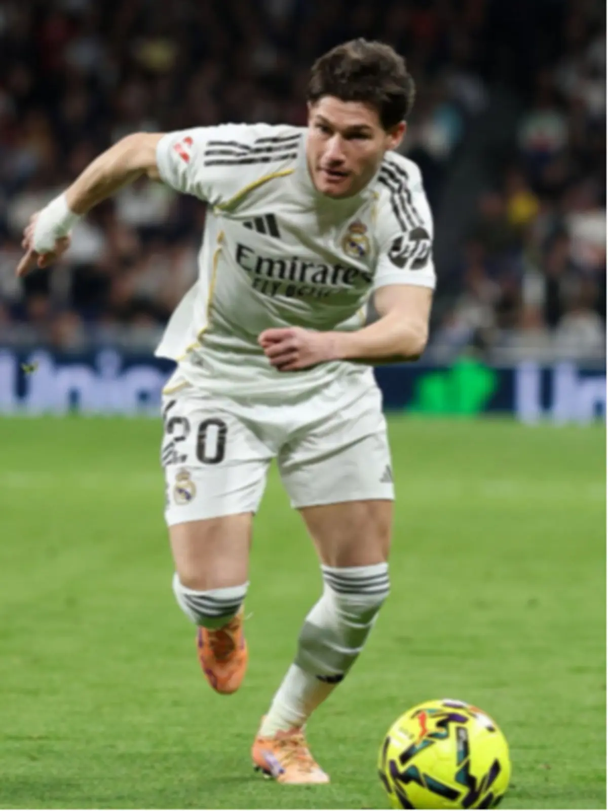 Futbolista del Reial Madrid amb el dorsal 20 corrent i controlant una pilota groga durant un partit a l’estadi