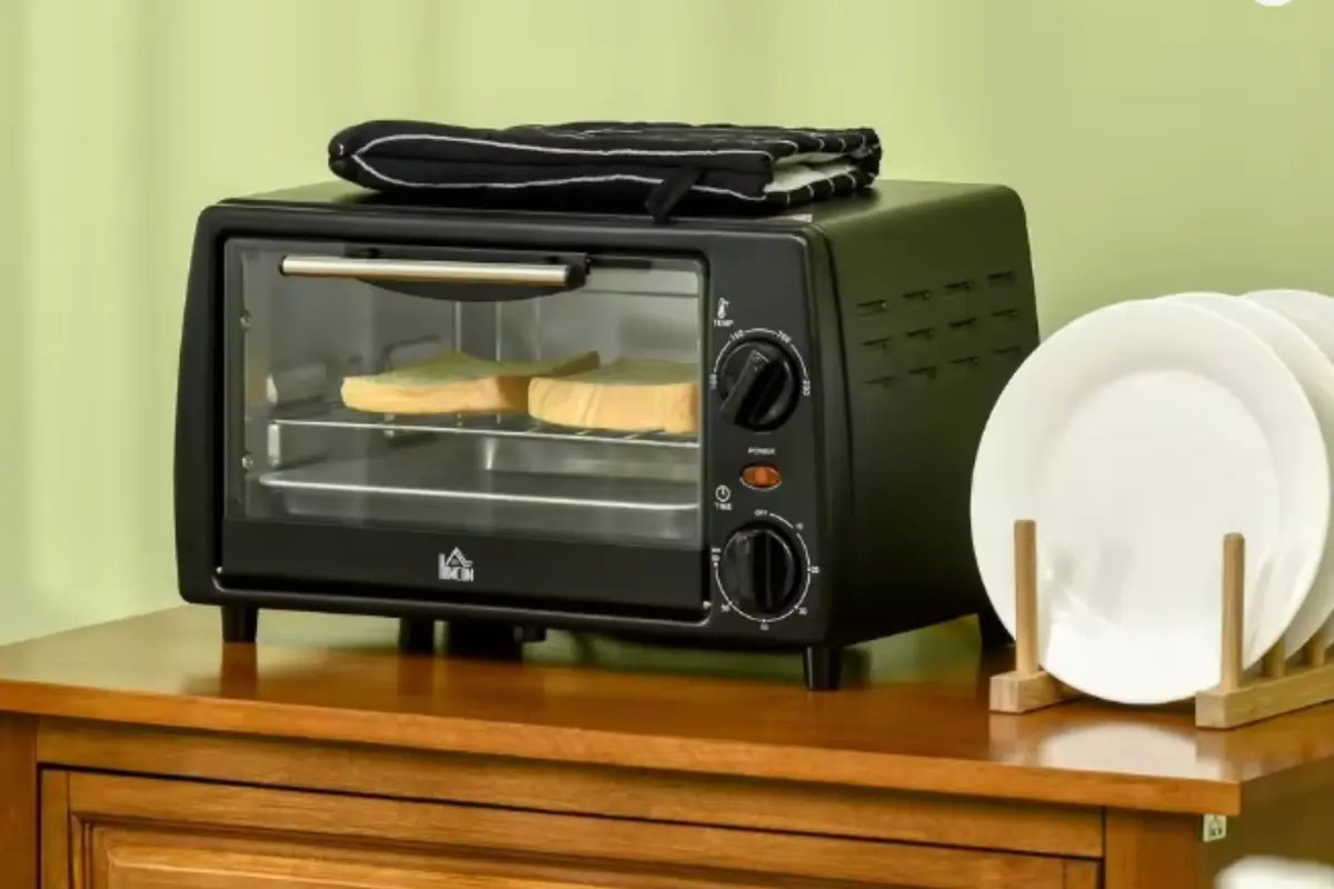 Horno negro sobre una mesa de madera con rebanadas de pan en su interior y un juego de platos blancos a un lado