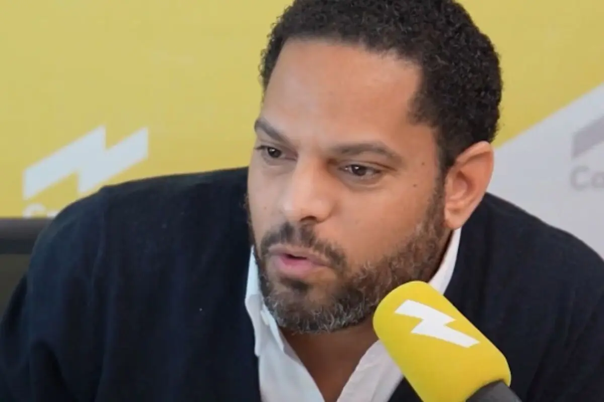 Hombre hablando frente a un micrófono amarillo en un estudio de radio con fondo amarillo