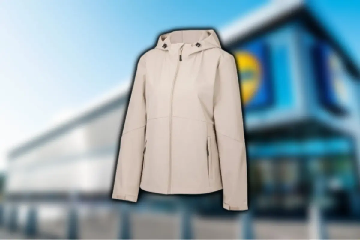 Jaqueta beix amb caputxa i cremallera frontal sobre un fons desenfocat d’edifici comercial