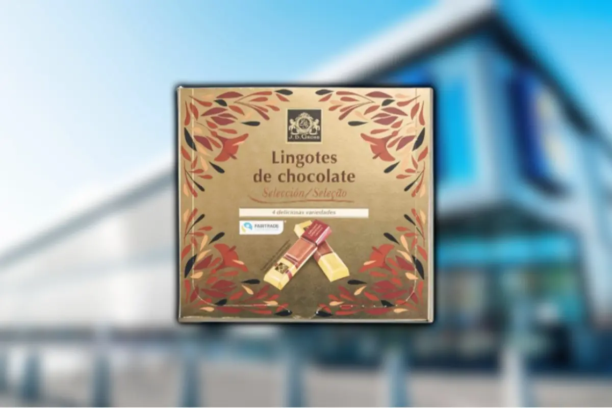 Golden box of assorted J. D. Gross chocolate bars with a red and black leaf design against a blurred supermarket background