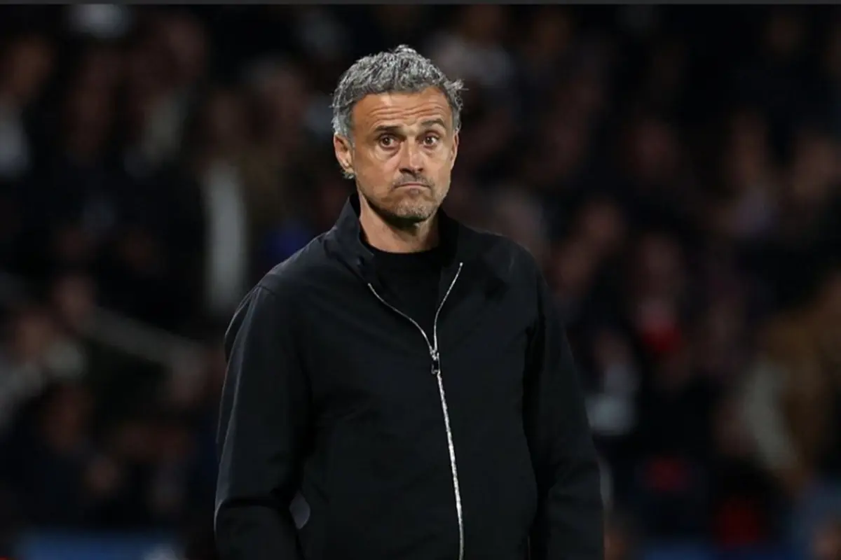 Entrenador de futbol de mitjana edat amb jaqueta negra mirant seriós durant un partit en un estadi ple