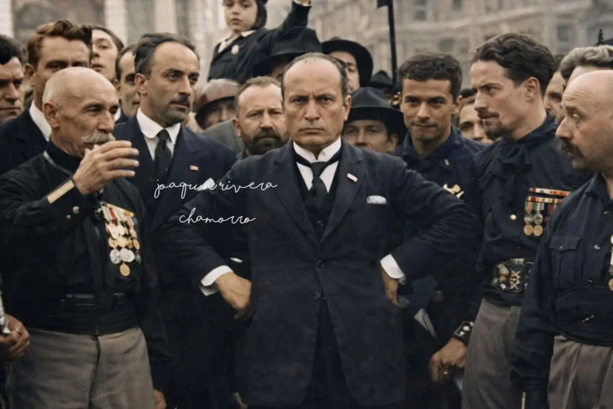 Home amb vestit fosc al centre d’una multitud de militars amb medalles en un acte públic històric; es tracta de la marxa sobre Roma amb Mussolini i les camises negres.