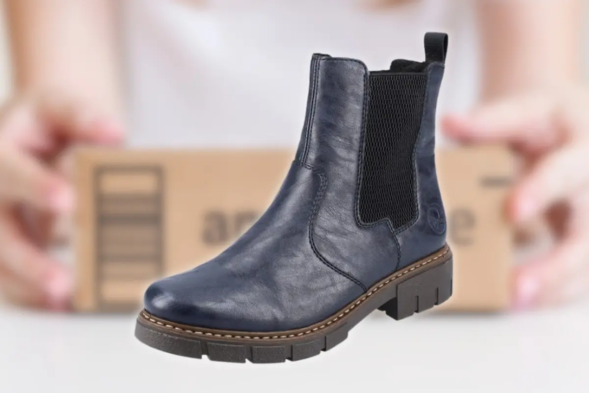 Botín tipo chelsea de cuero azul marino con suela gruesa frente a un paquete de envío sostenido por una persona
