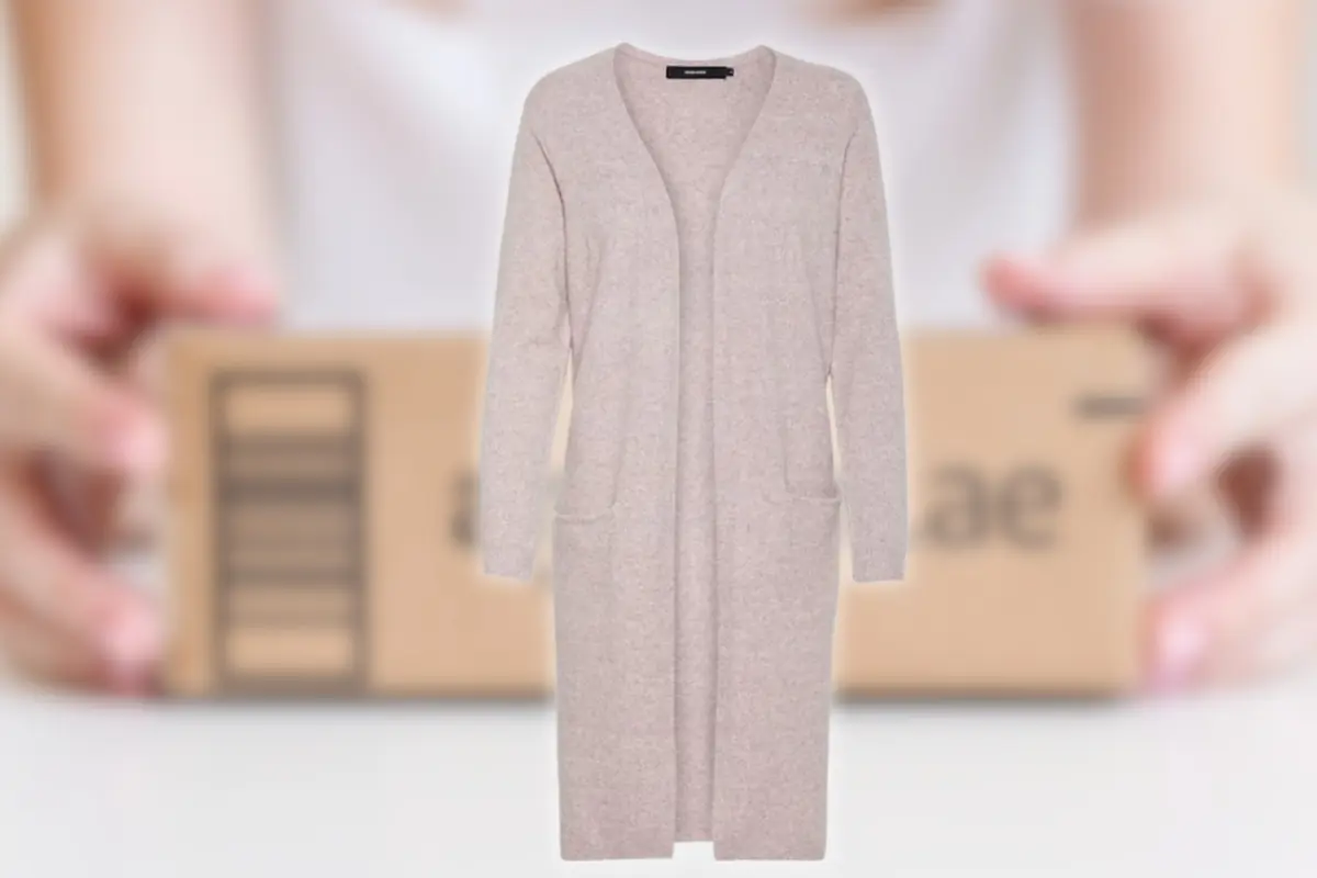 Cárdigan largo de punto beige claro con bolsillos delanteros sobre fondo desenfocado de un paquete de envío sostenido por unas manos