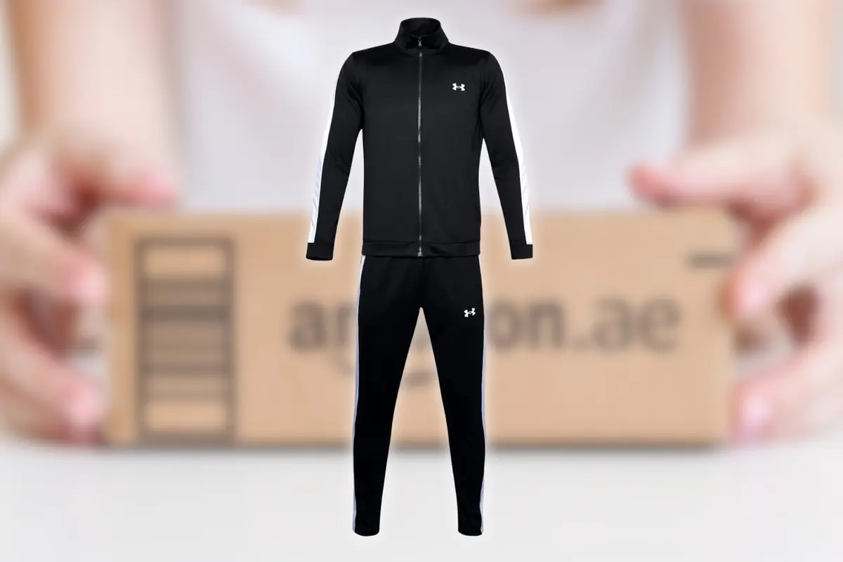 Chándal negro deportivo con franjas blancas en las mangas y laterales del pantalón sobre fondo desenfocado con caja de envío de Amazon