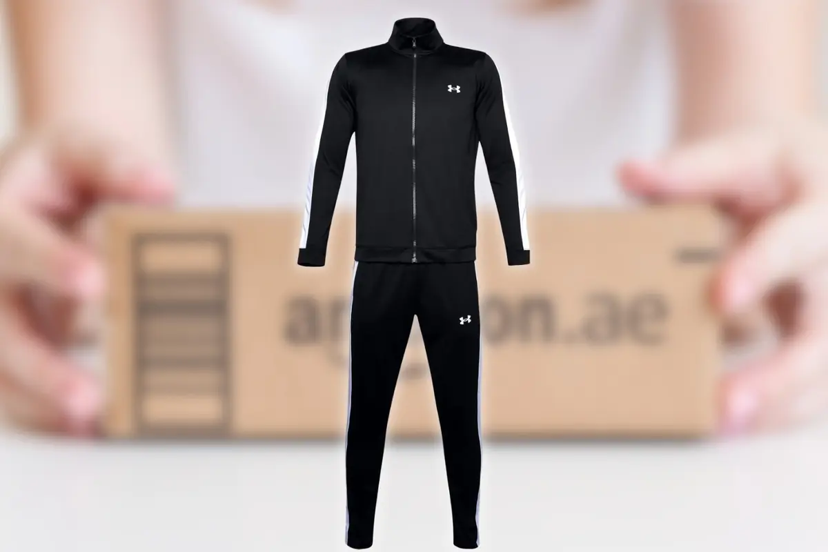 Chándal negro deportivo Under Armour con franjas blancas en las mangas y laterales del pantalón sobre fondo de paquete de envío desenfocado