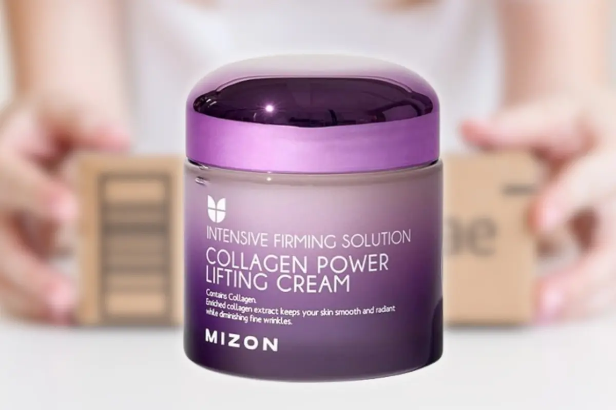 Tarro morado de crema facial Mizon Collagen Power Lifting Cream en primer plano con manos sosteniendo cajas desenfocadas al fondo