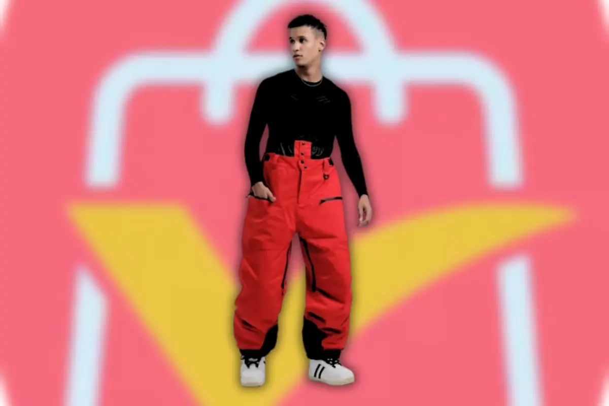 Joven con pantalones rojos anchos y sudadera negra posando sobre fondo rosa con icono de bolsa de compras estilizada