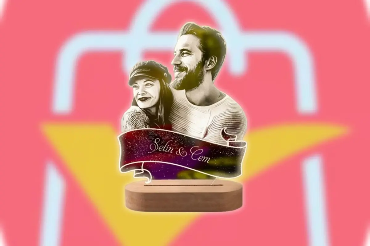 Lámpara decorativa con ilustración de pareja abrazada y cinta con los nombres Selin & Cem sobre base de madera con el logo de AliExpress desenfocado como fondo