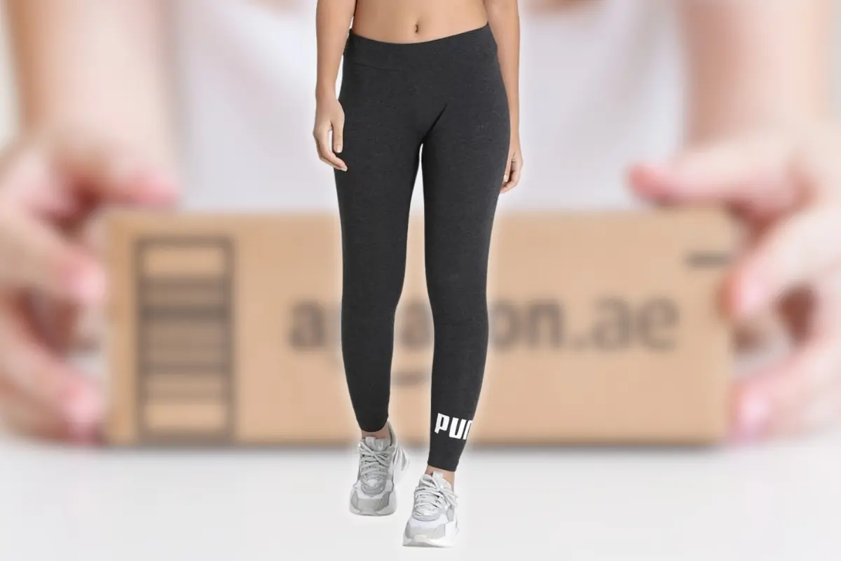 Mujer con mallas deportivas negras Puma y zapatillas grises frente a una caja de envío de Amazon desenfocada