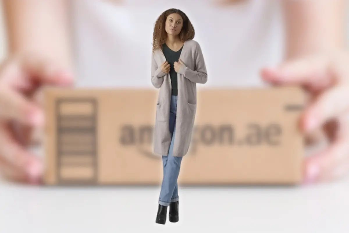 Mujer joven con cárdigan gris y jeans de pie frente a una caja de envío de Amazon desenfocada en segundo plano