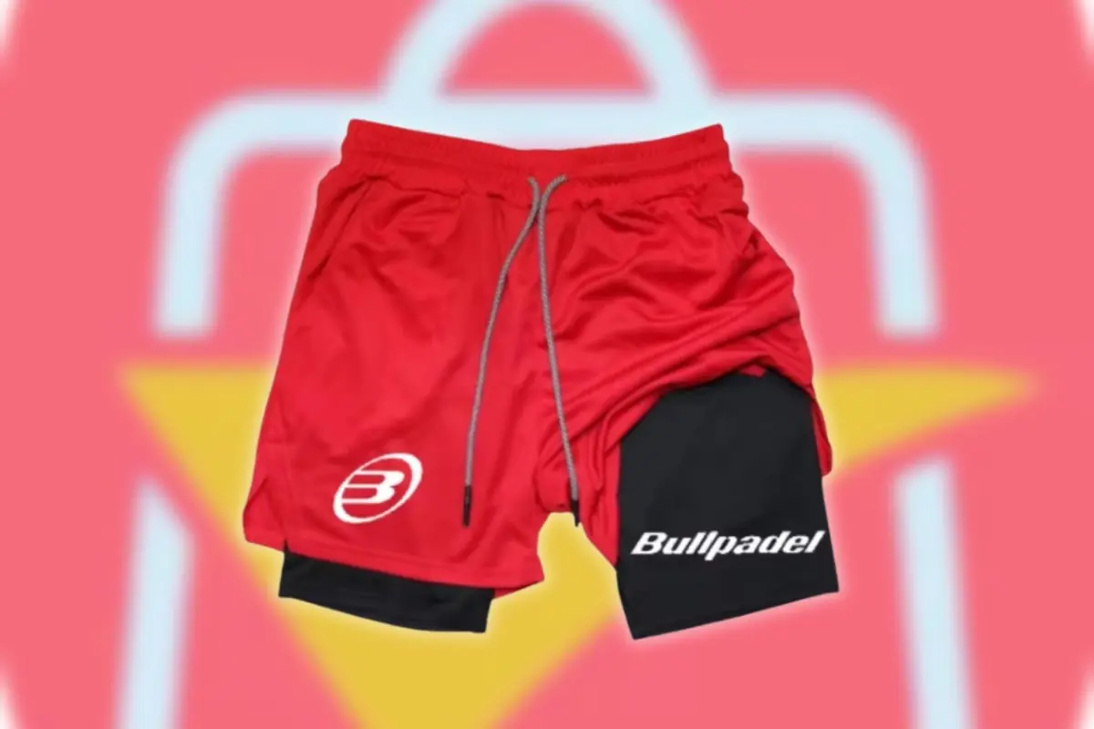Pantalón corto deportivo rojo con malla interior negra y logotipo Bullpadel sobre fondo desenfocado del logo de AliExpress