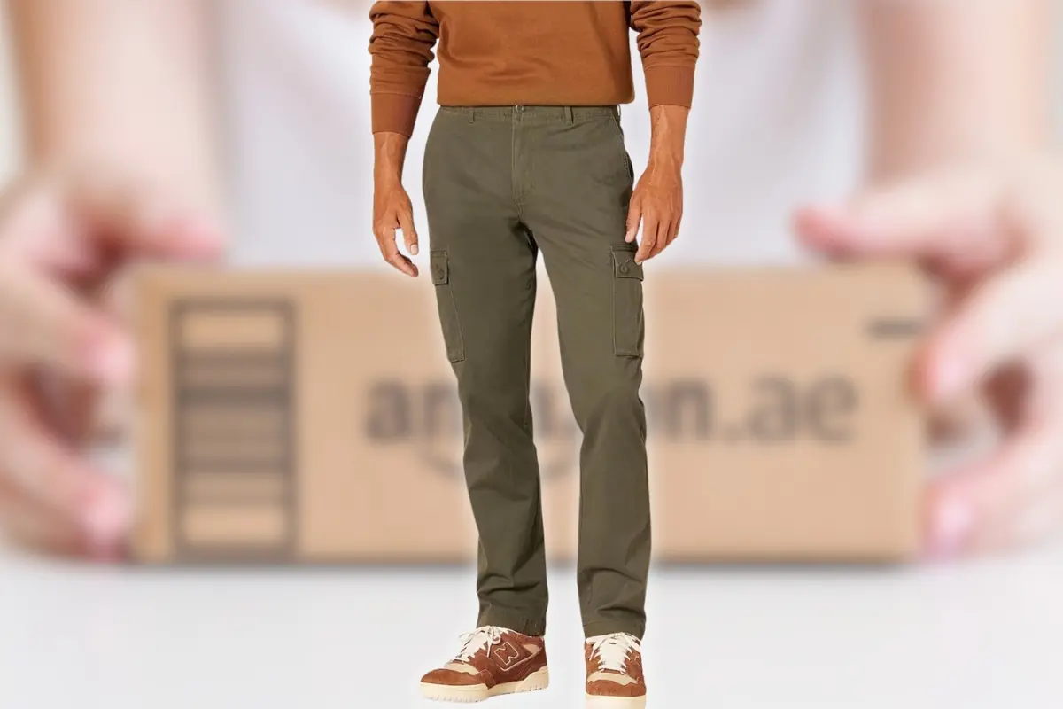 Hombre con pantalones cargo verdes y suéter marrón posando frente a una caja de envío de Amazon
