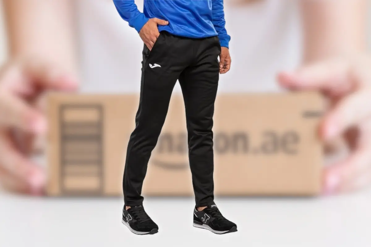 Hombre con sudadera azul y pantalones deportivos negros posando frente a una caja de envío de Amazon desenfocada