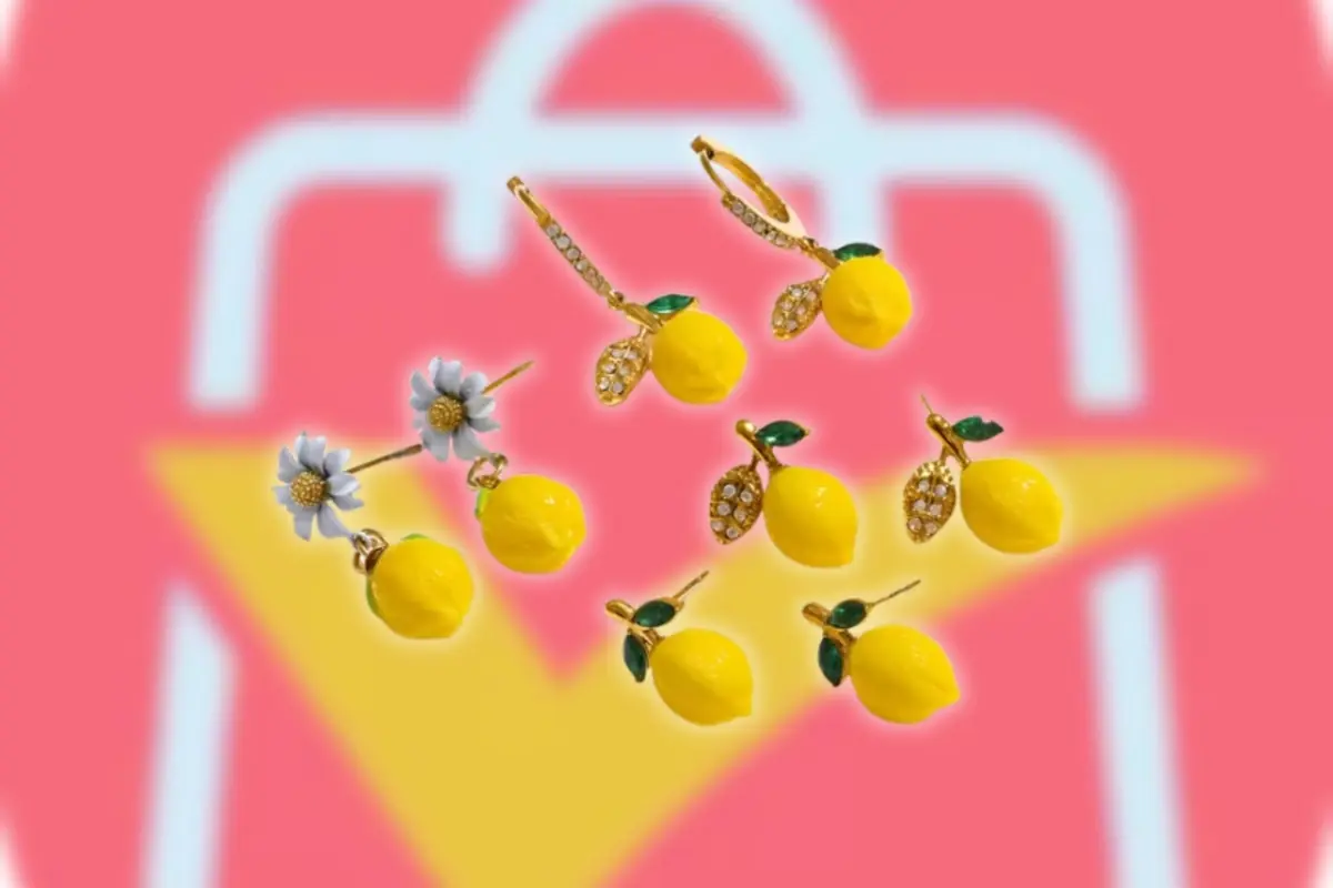 Pendientes dorados con dijes de limón amarillo y flores blancas sobre fondo con el logo de AliExpress desenfocado
