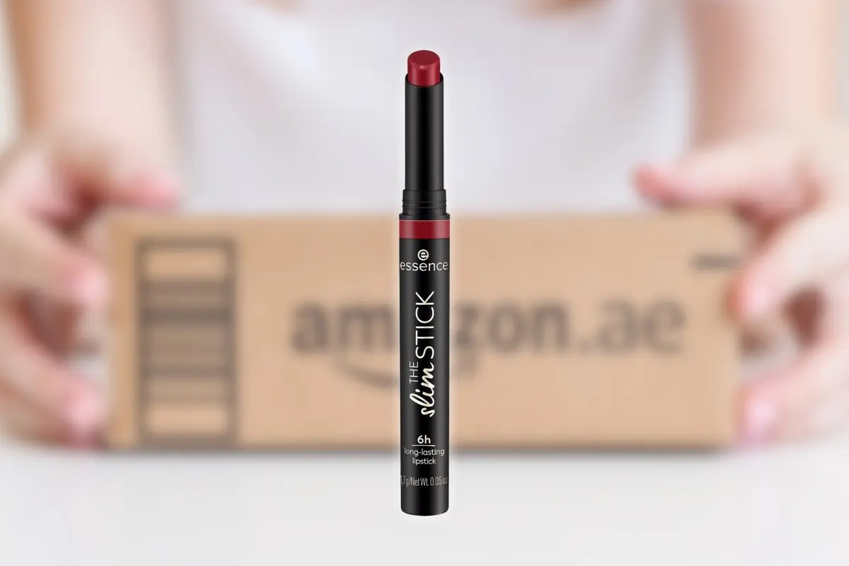 Barra de labial rojo Essence The Slim Stick en primer plano con una caja de envío de Amazon desenfocada al fondo