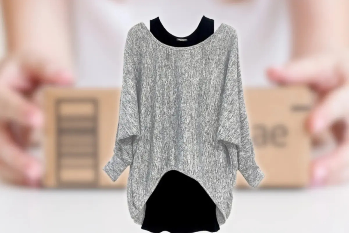 Pullover gris holgado de manga larga sobre fondo desenfocado con caja de envío en manos humanas