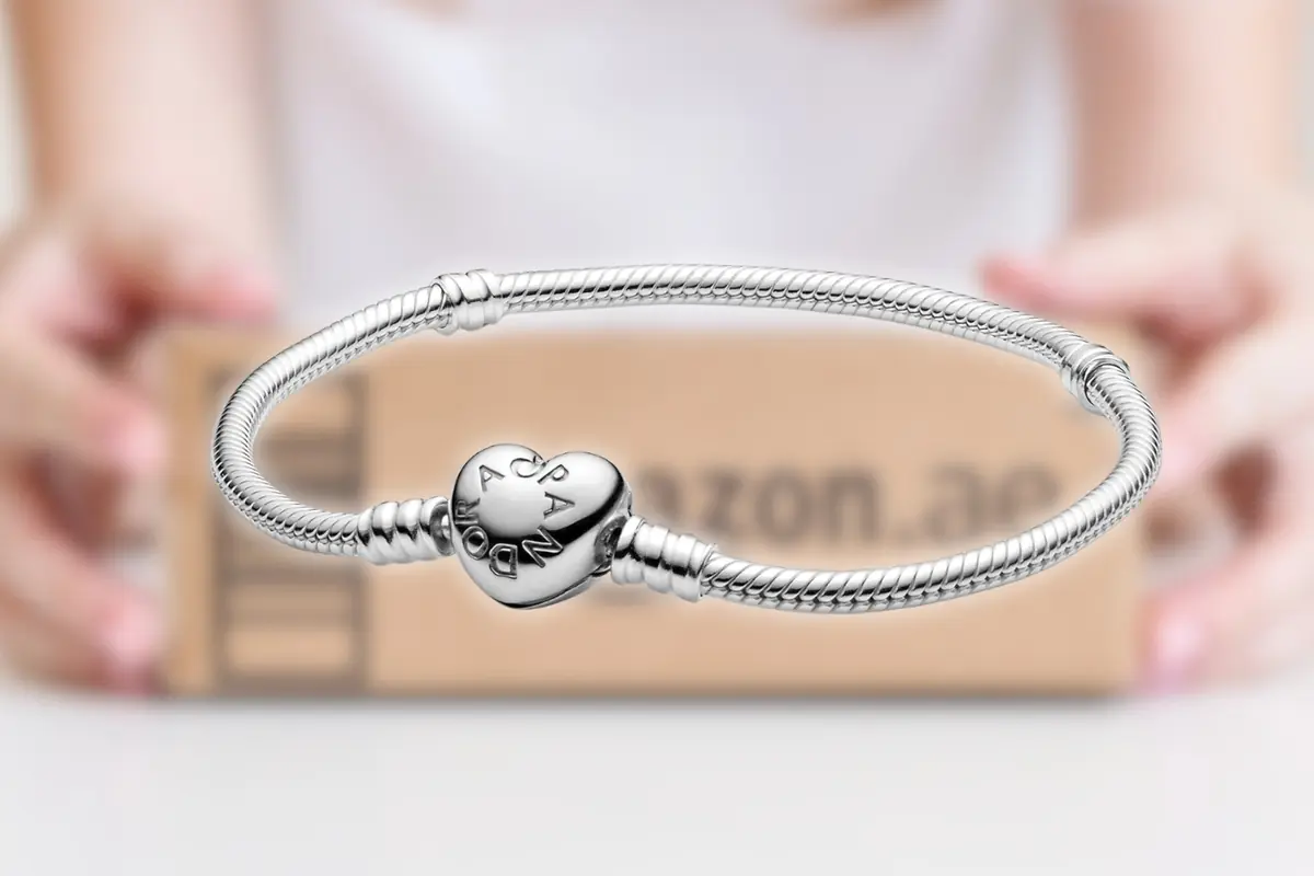 Pulsera plateada tipo Pandora con cierre en forma de corazón enfocada frente a una caja de envío de Amazon