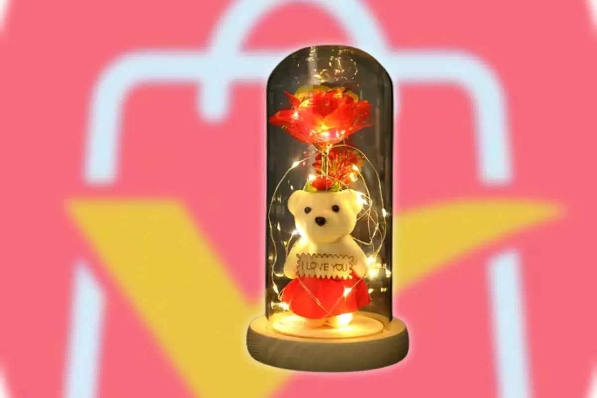 Osito de peluche con letrero I love you y rosa roja iluminados dentro de una cúpula de cristal sobre base de madera con el logo desenfocado de AliExpress