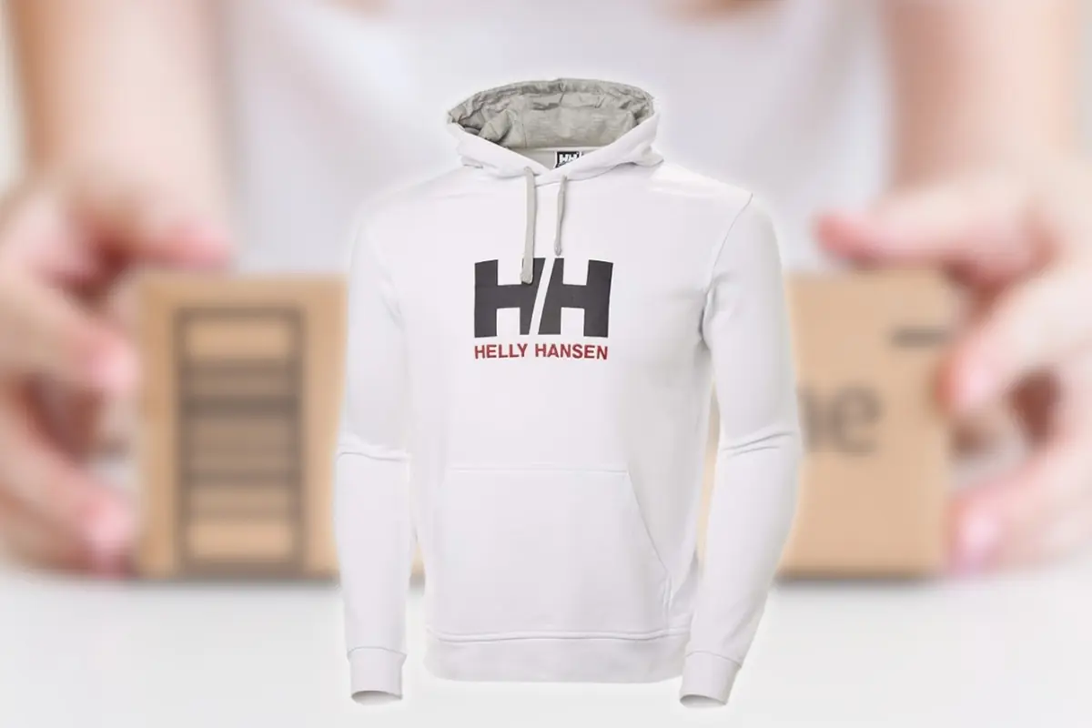 Sudadera con capucha blanca Helly Hansen con logo HH en el pecho sobre fondo desenfocado con manos sosteniendo una caja de cartón