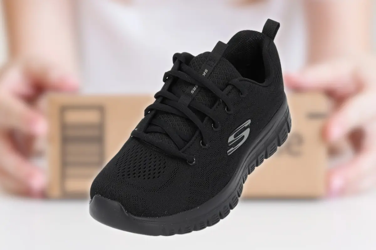 Zapatilla deportiva negra con cordones y suela gruesa en primer plano sobre fondo desenfocado con caja de envío detrás