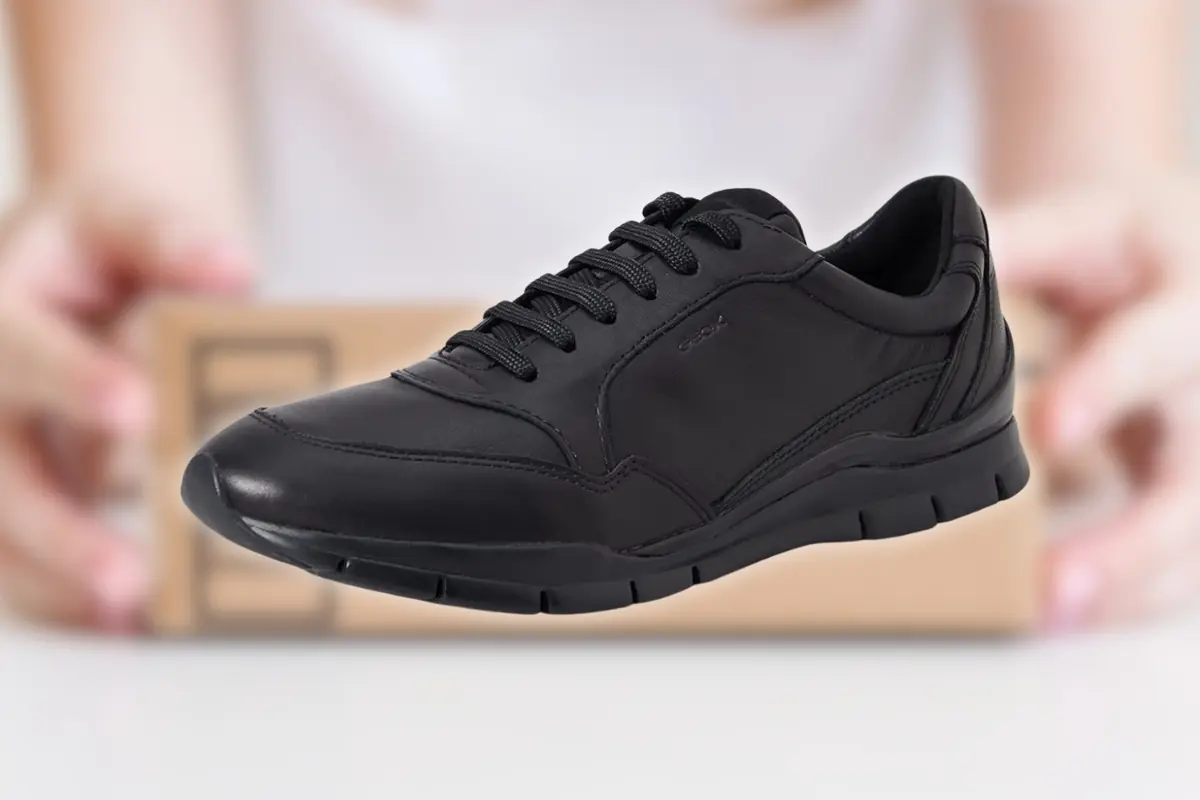 Zapato deportivo negro de piel con cordones sobre fondo desenfocado con caja de envío detrás