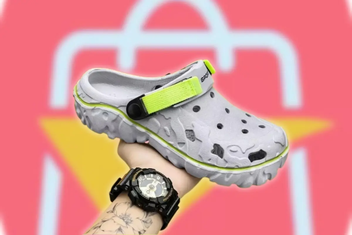 Mano de hombre sosteniendo en su mano un zueco gris, teniendo como fondo el logo de AliExpress desenfocado