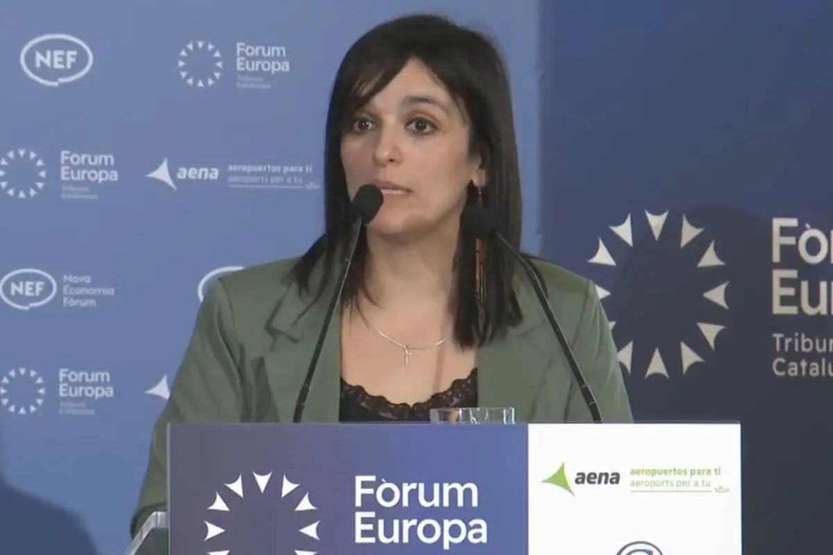 Dona parlant davant de dos micròfons en un faristol del Fòrum Europa amb un fons blau ple de logotips