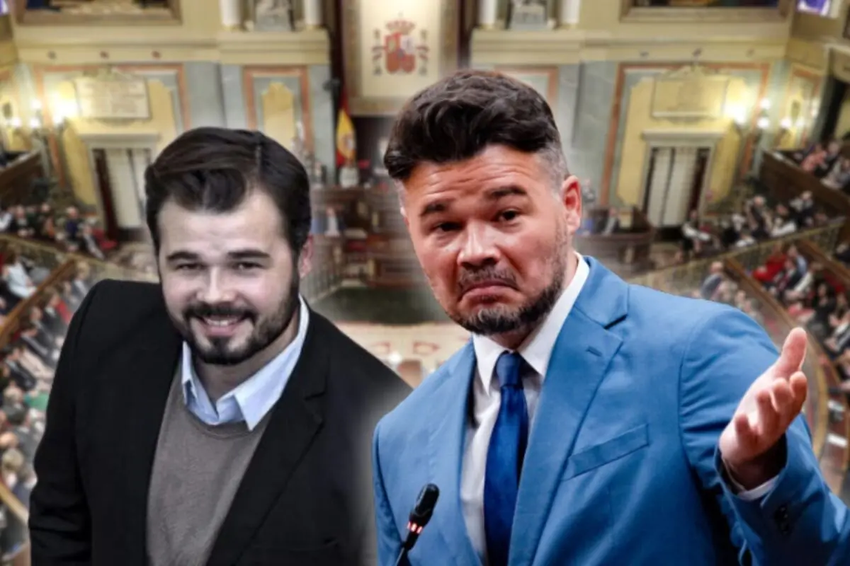 Dos homes de mitjana edat amb barba en primer pla sobre el fons d’un parlament ple de gent, un amb vestit fosc somrient i l’altre amb vestit blau gesticulant davant d’un micròfon