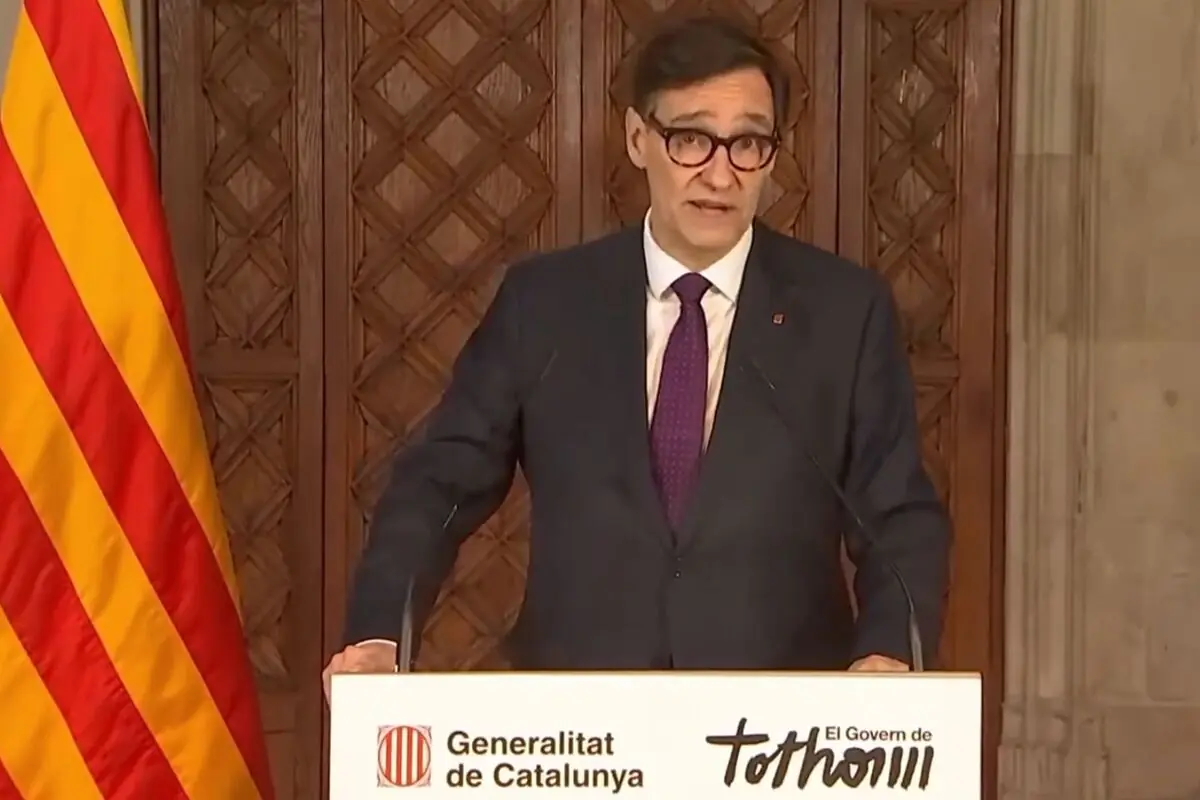 Home amb ulleres i vestit fent un discurs en un faristol de la Generalitat de Catalunya al costat d’una bandera catalana