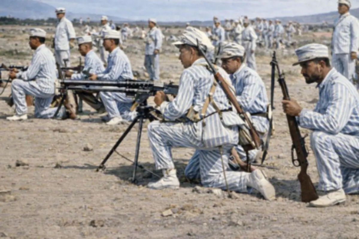 Soldats amb uniformes de ratlles entrenant amb metralladores i fusells en un camp obert.