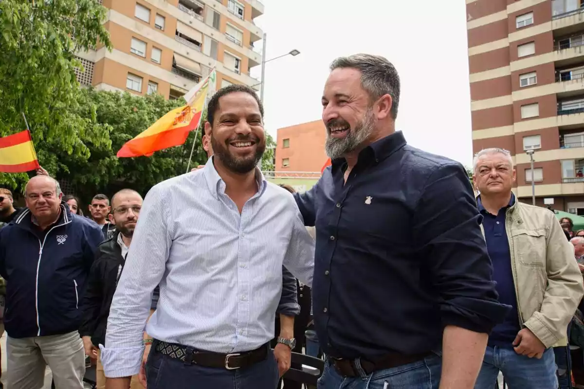Pla mitjà d'Ignacio Garriga i Santiago Abascal rient en una plaça de Salt amb desenes de simpatitzants darrere