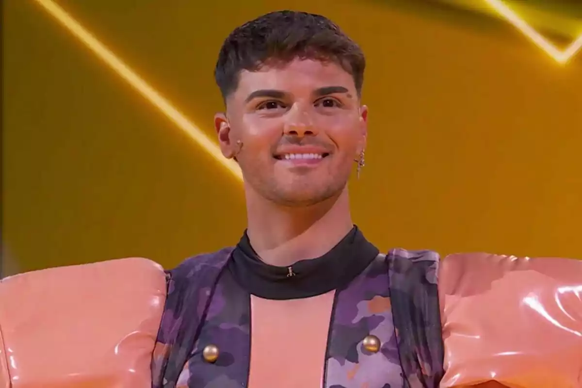 Abraham Mateo somrient amb un vestit colorit i muscleres grans en un fons groc a Mask Singer.