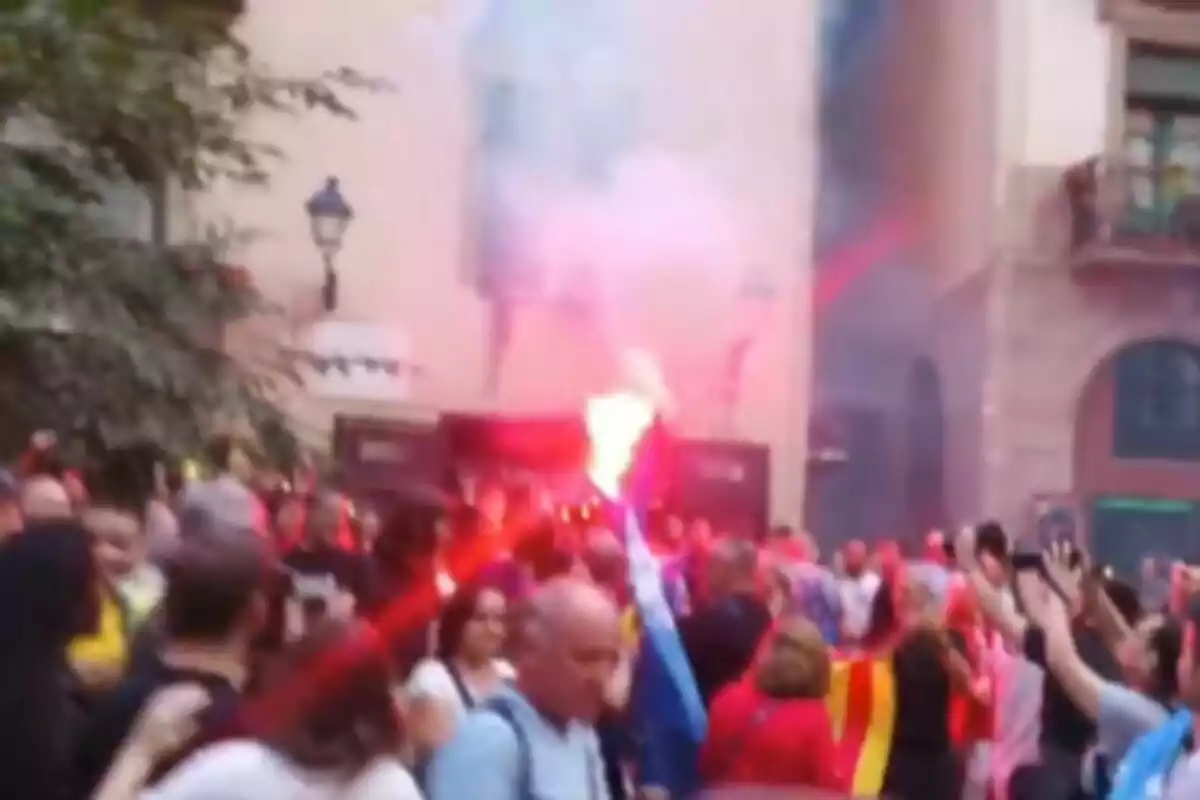 Una multitud de persones en una manifestació amb bengales i banderes a un carrer.