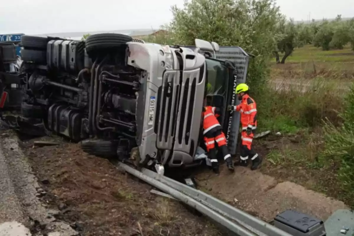 Un camió bolcat a la carretera amb dues persones de rescat treballant a l'escena.